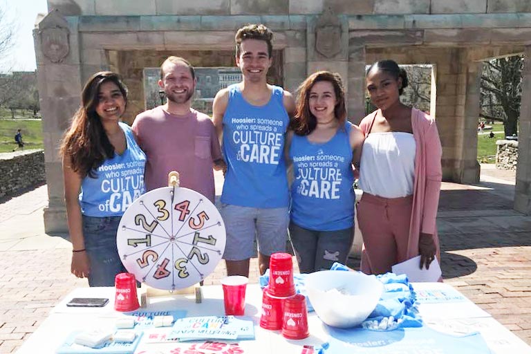 students wearing shirts that say culture of care, standing behind a table with papers and a game wheel on it