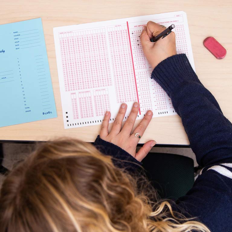 a person leaning over a testing sheet, filling in an answer