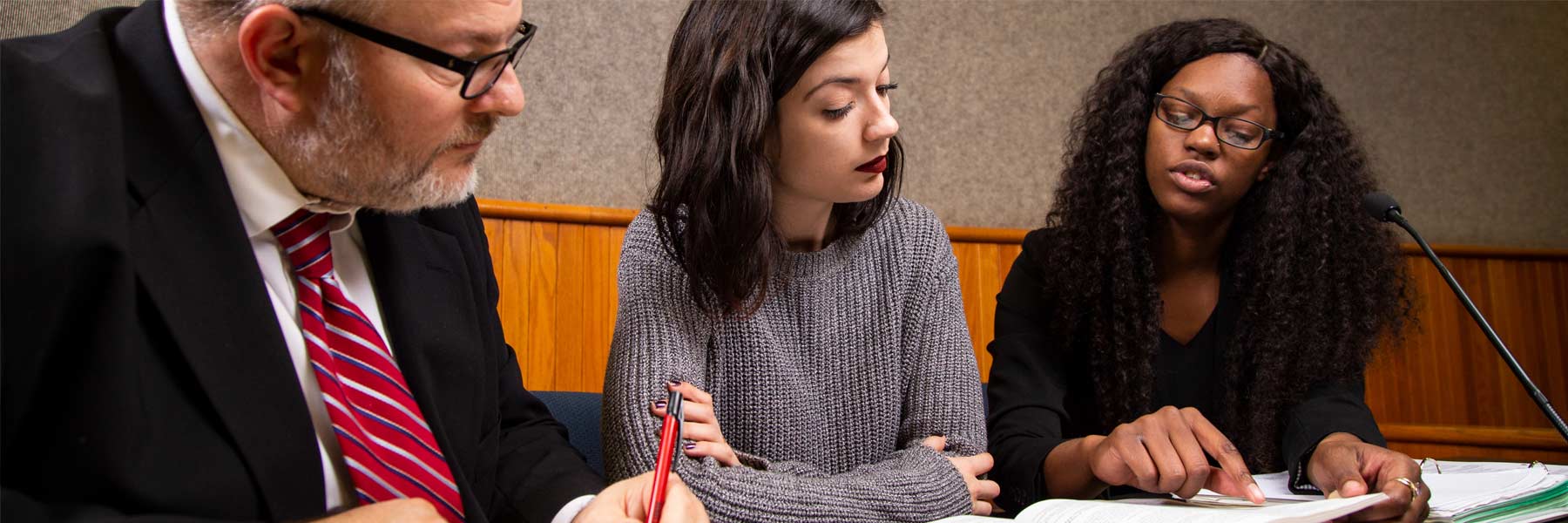 a man and two women sitting together at a table, looking at papers. One woman is pointing at the papers and talking